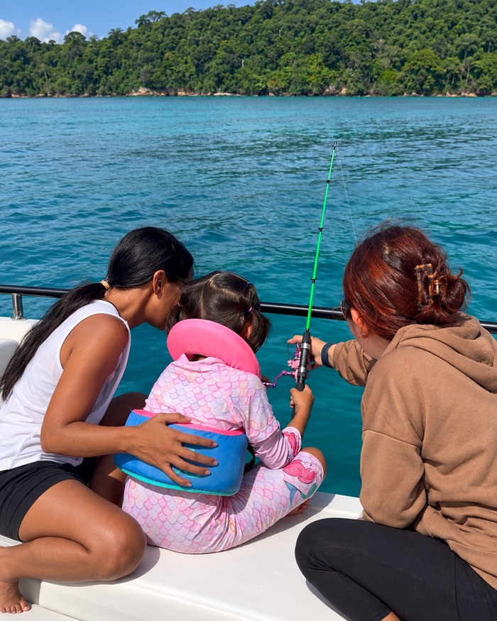 A child fishing from the boat with both adults fully visible beside her