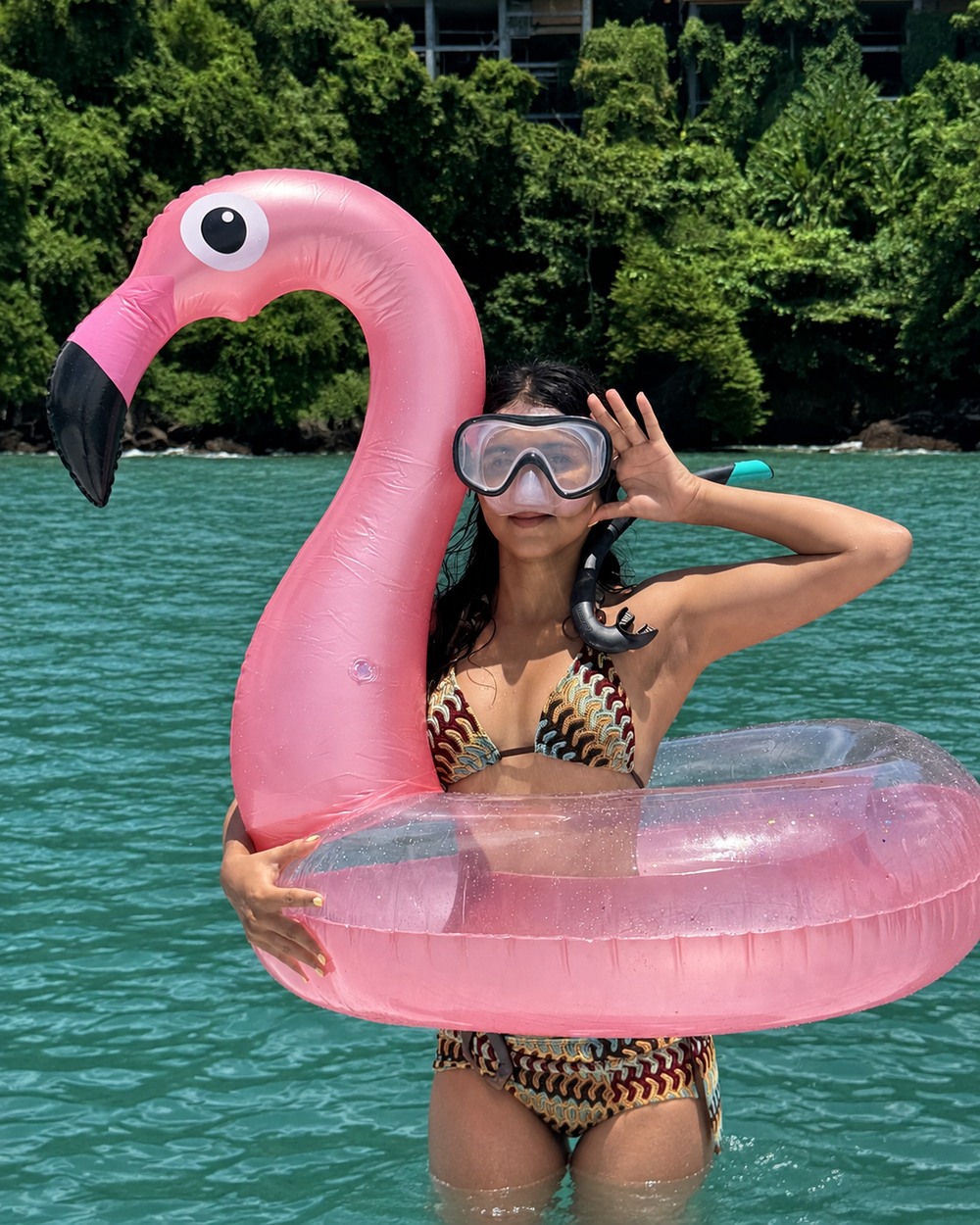 A guest wearing a snorkel mask and holding a complete pink flamingo float in turquoise water