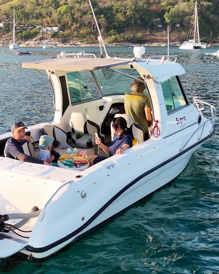 A family sharing fruit aboard an AquaTour boat in a calm Phuket bay