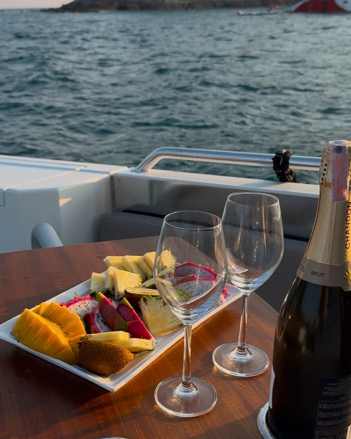 Fresh tropical fruit, two glasses and a bottle of champagne served on board at sunset