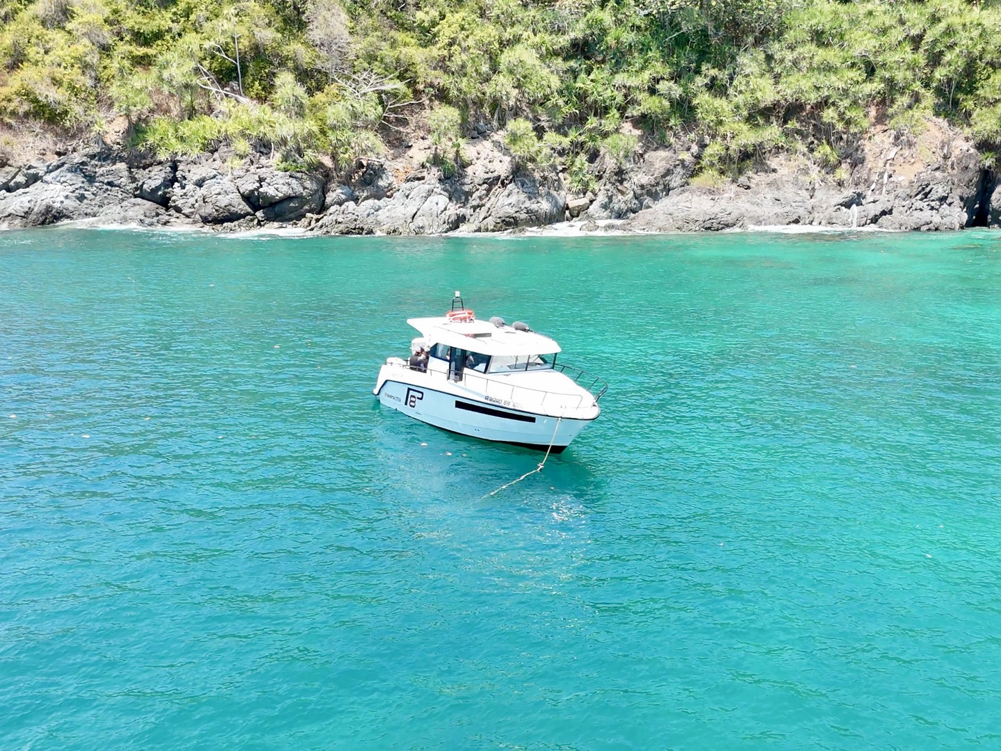 Finnmaster Pilot anchored in an emerald cove below a green cliff