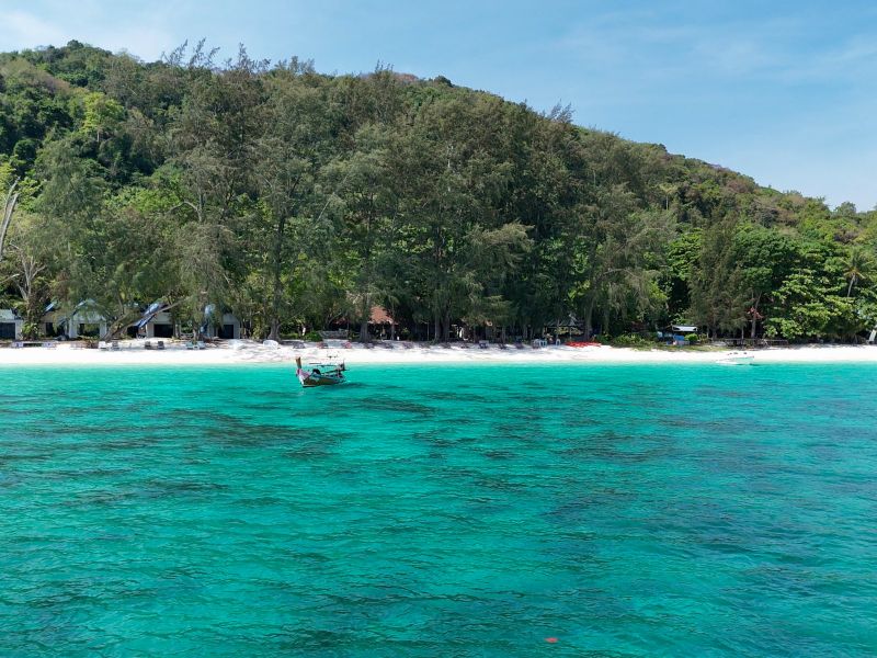 A longtail boat resting in clear turquoise shallows off the white-sand beach at Coral Island