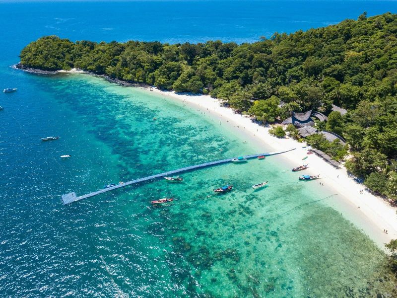 Aerial view of the floating pontoon pier reaching across the reef to the beach at Coral Island