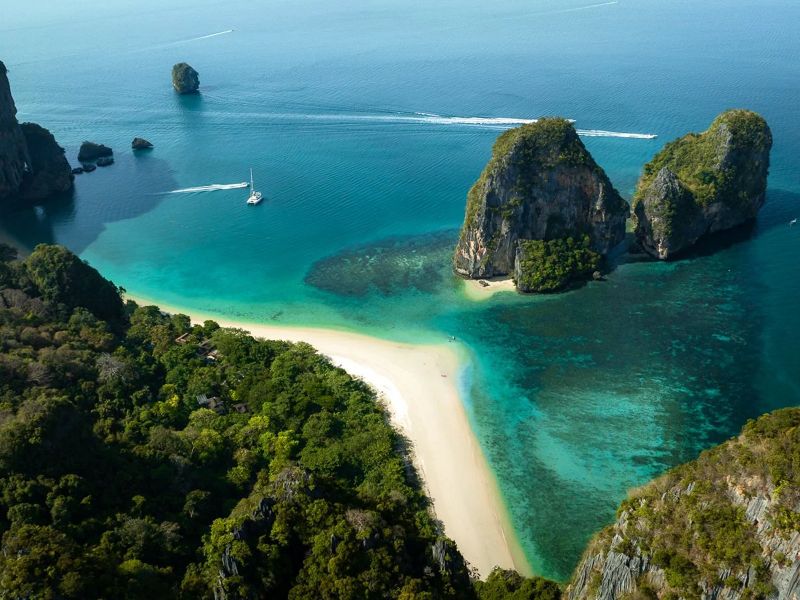 Aerial view of a sandbar linking green karst islands over clear turquoise reef near Koh Ngai