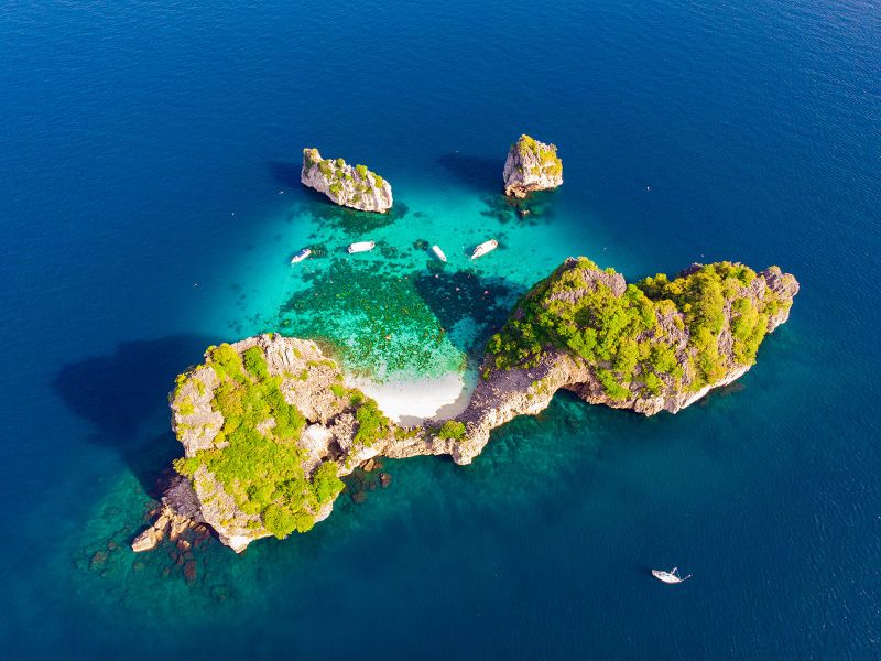 Aerial view of the Koh Rok islands with dive boats moored over a bright turquoise reef lagoon