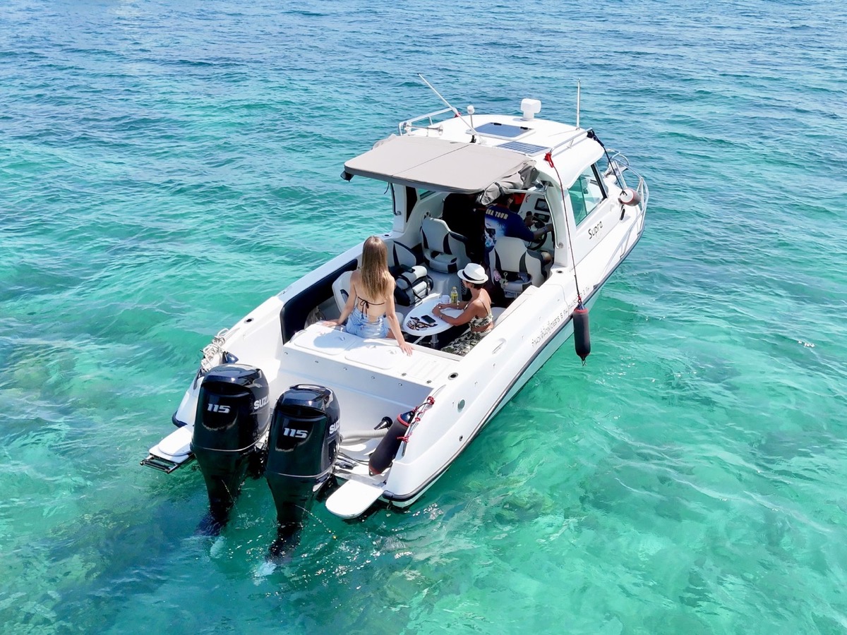 People seated around the table on the rear deck of Atomix 705HT in clear turquoise water.