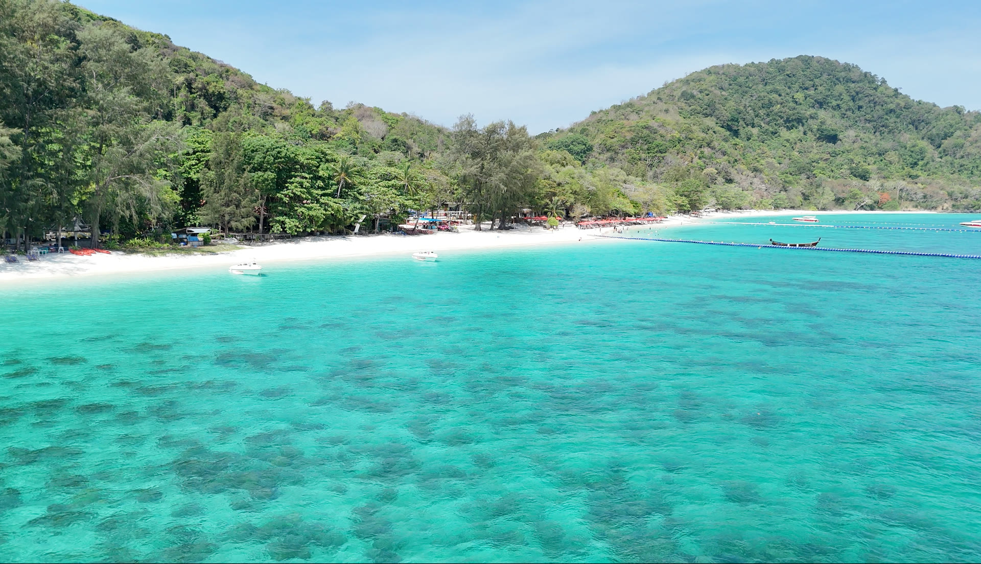 Aerial view of a forested island beach and turquoise reef near Phuket